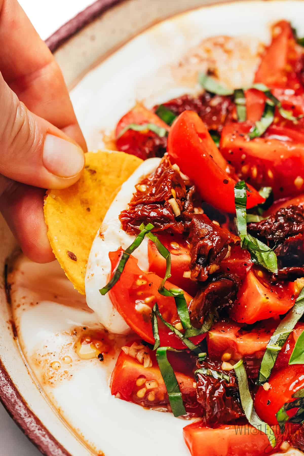 Bruschetta dip being scooped with a cracker.