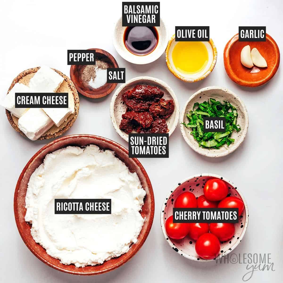 Labeled bruschetta dip ingredients: ricotta cheese, cream cheese, olive oil, sea salt, cherry tomatoes, sun-dried tomatoes, fresh basil, garlic, balsamic vinegar, and black pepper.