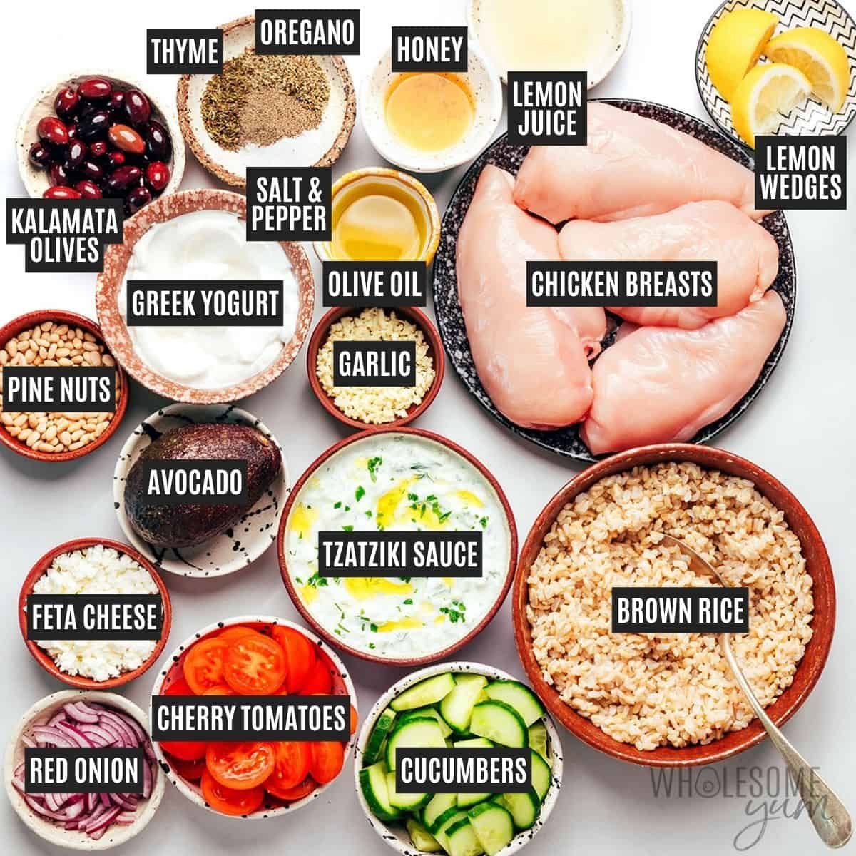 Labeled bowl ingredients: Yogurt marinated chicken ingredients, brown rice, veggies, olives, avocado, feta cheese, pine nuts, tzatziki sauce, and lemon wedges.