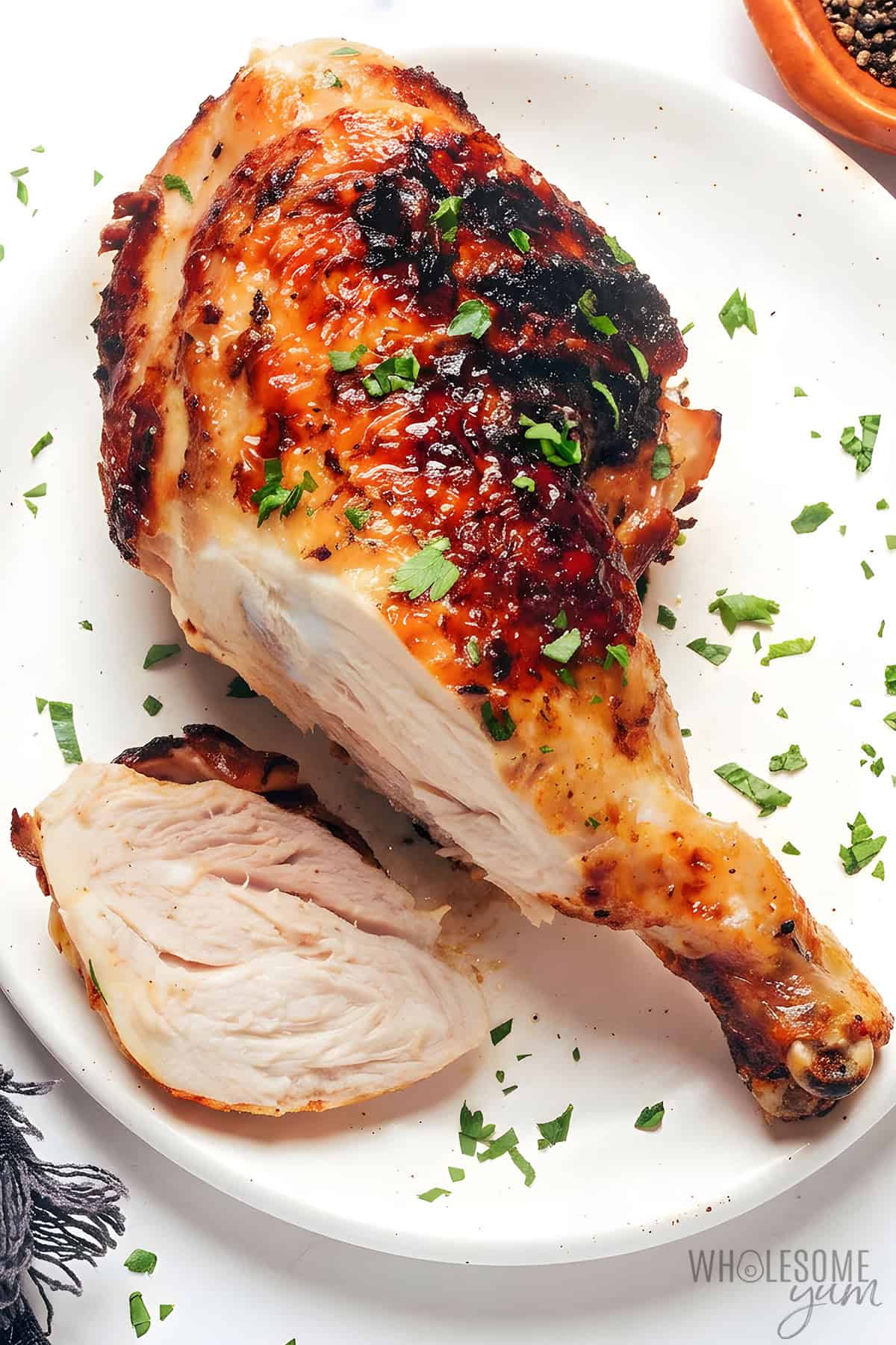Golden brown grilled chicken leg quarter on a plate with a slice cut to show the juicy inside.
