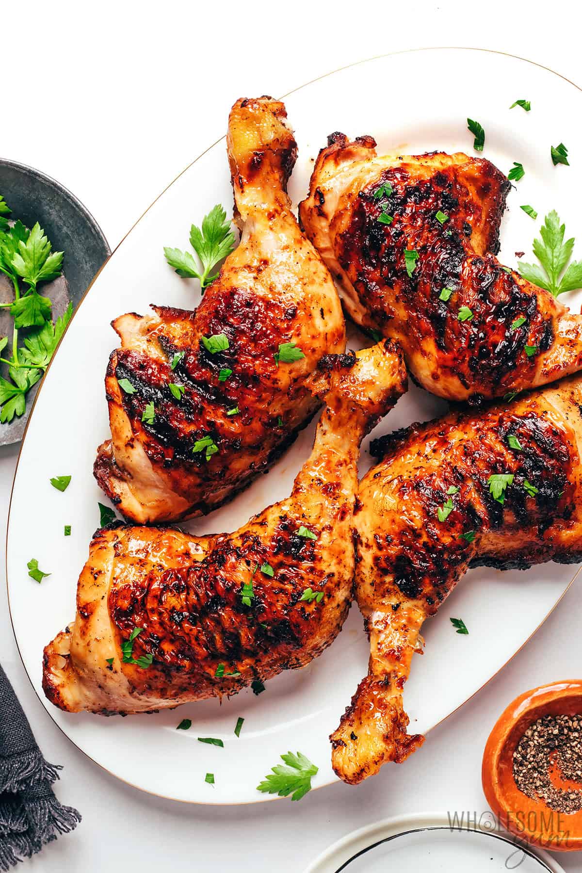Juicy, charred grilled chicken quarters on a platter with a sprinkle of fresh parsley.