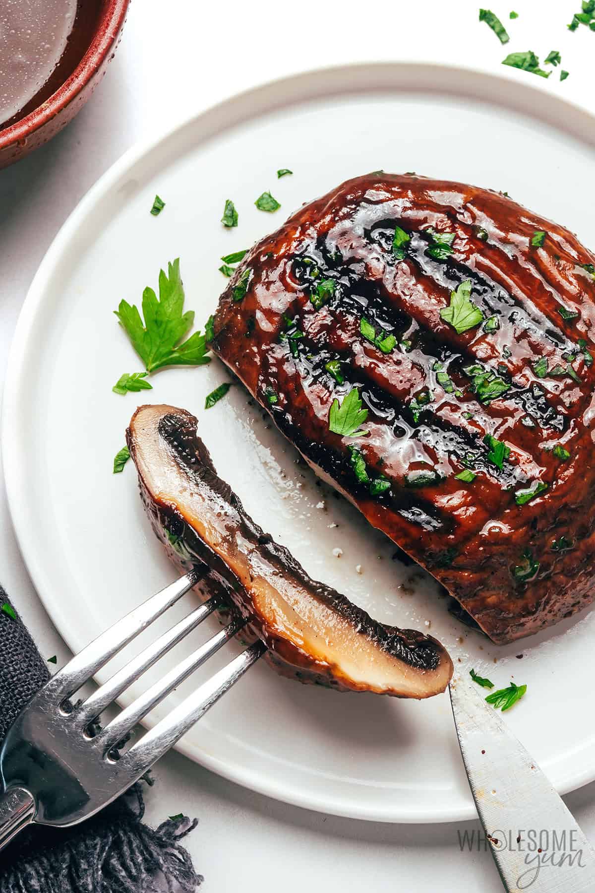 Grilled portobello mushroom on a plate, sliced with a fork to show the juicy texture inside.