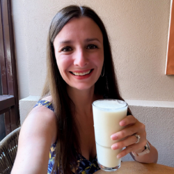 Maya holding a pineapple smoothie in a tall glass.
