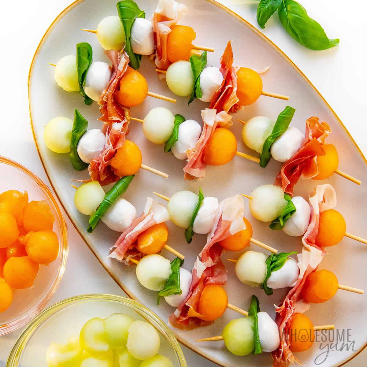 Prosciutto and melon skewers arranged on a serving plate.