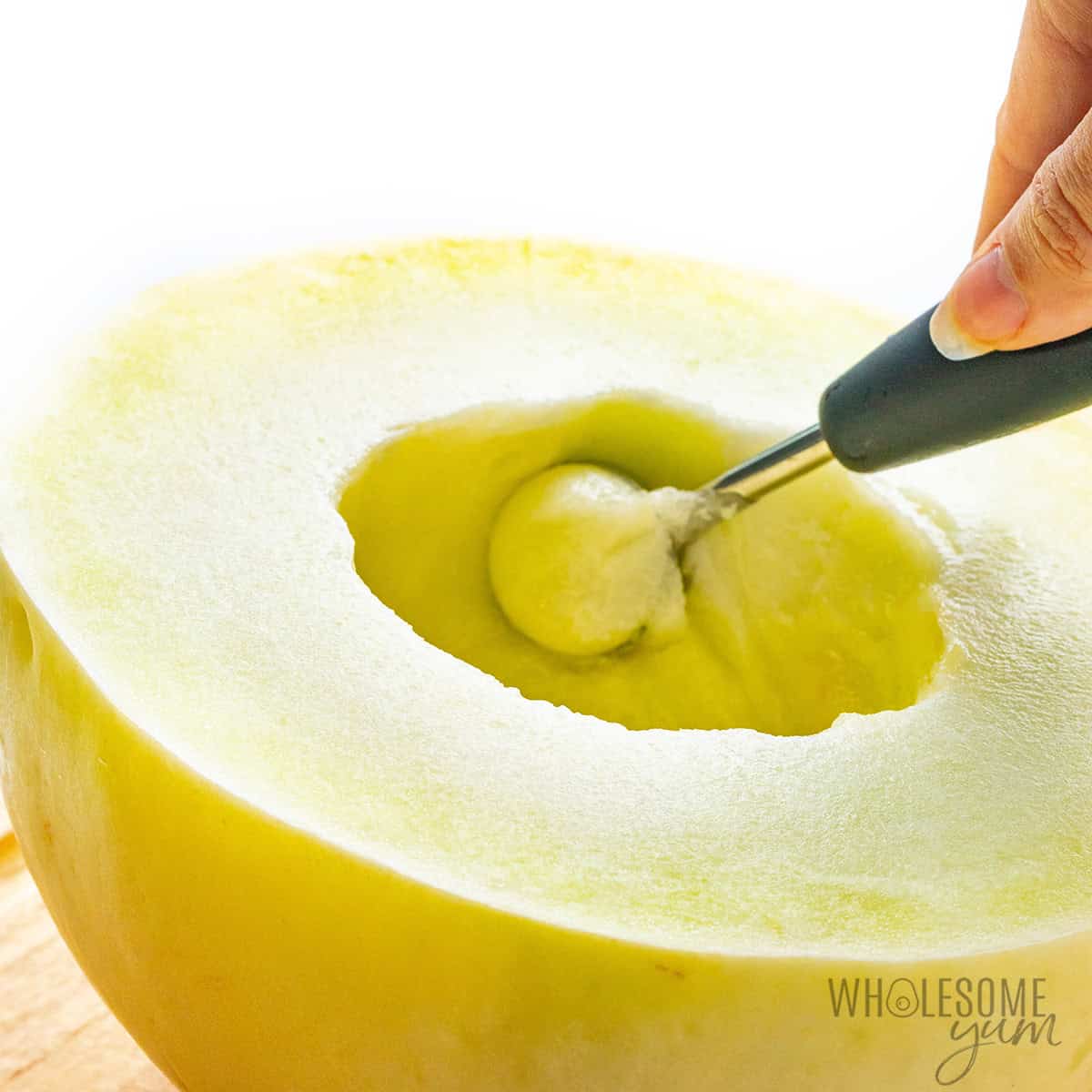 Melon baller lifting a round melon ball from a halved melon.