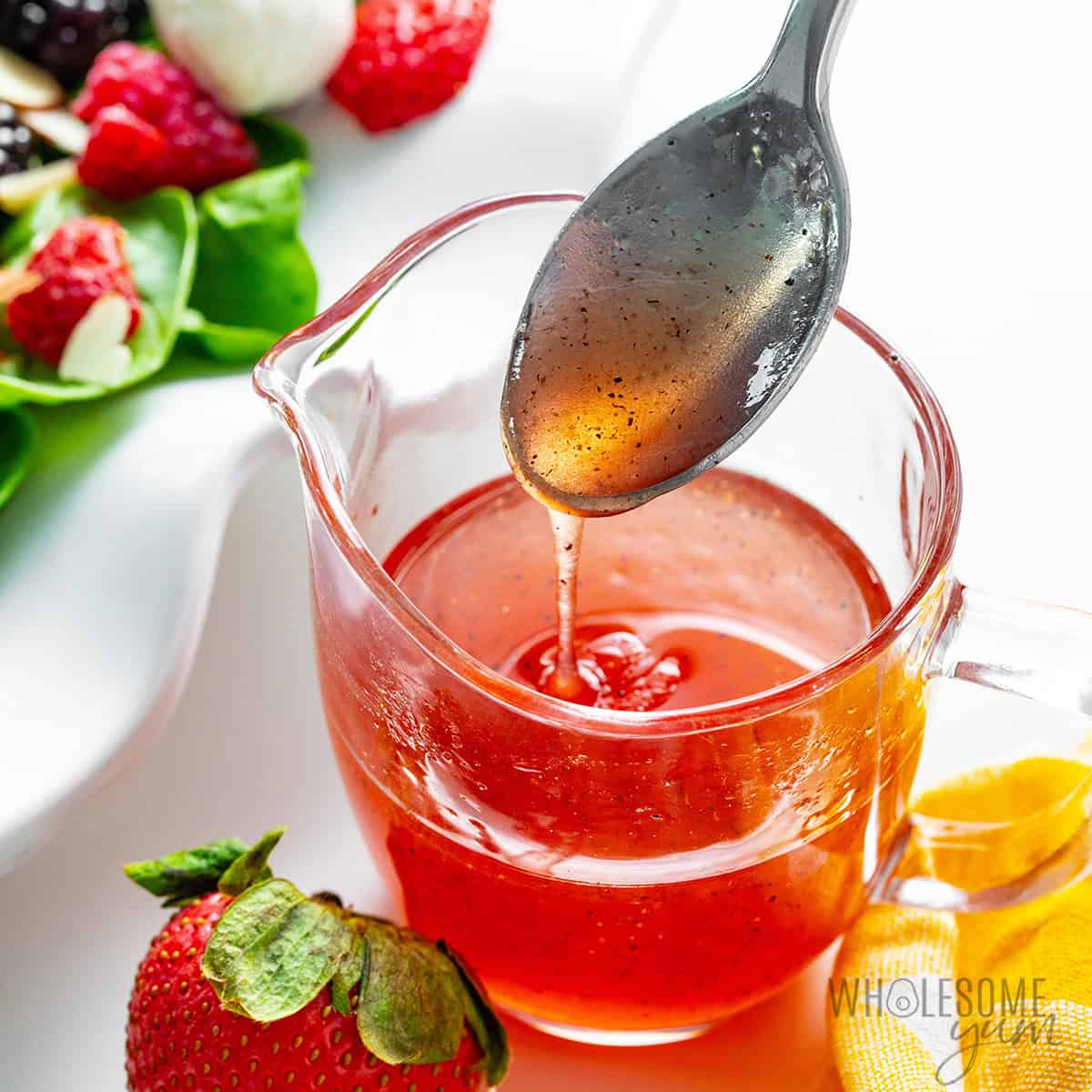Strawberry vinaigrette in a measuring cup with a spoon drizzling the dressing.