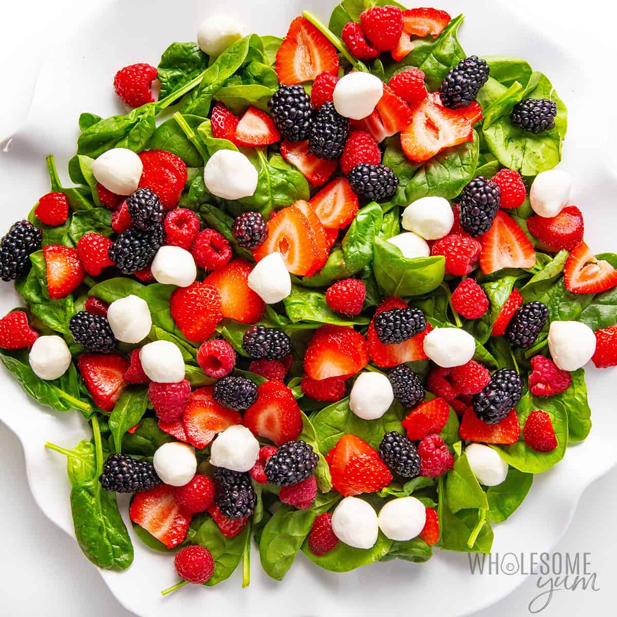 Fresh berries and mozzarella scattered over spinach on a platter.