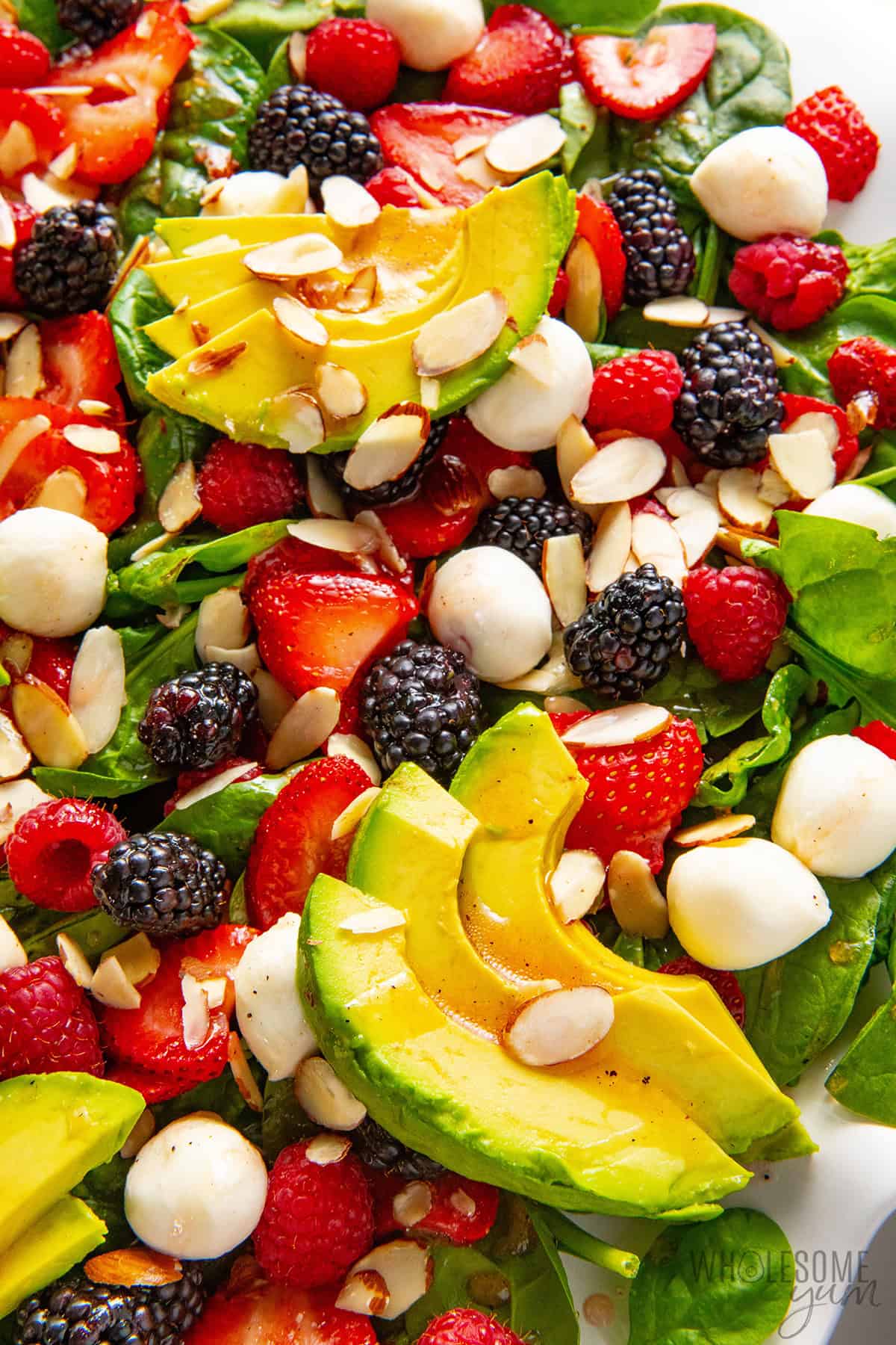Colorful, fresh summer salad up close with spinach, berries, mozzarella, avocado, and strawberry vinaigrette drizzled over it.