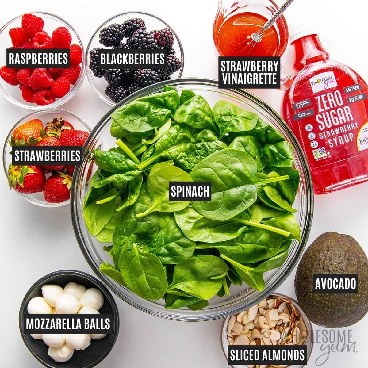 Labeled recipe ingredients: Fresh spinach, strawberries, raspberries, blackberries, fresh mozzarella balls, avocado, sliced almonds, and strawberry vinaigrette.