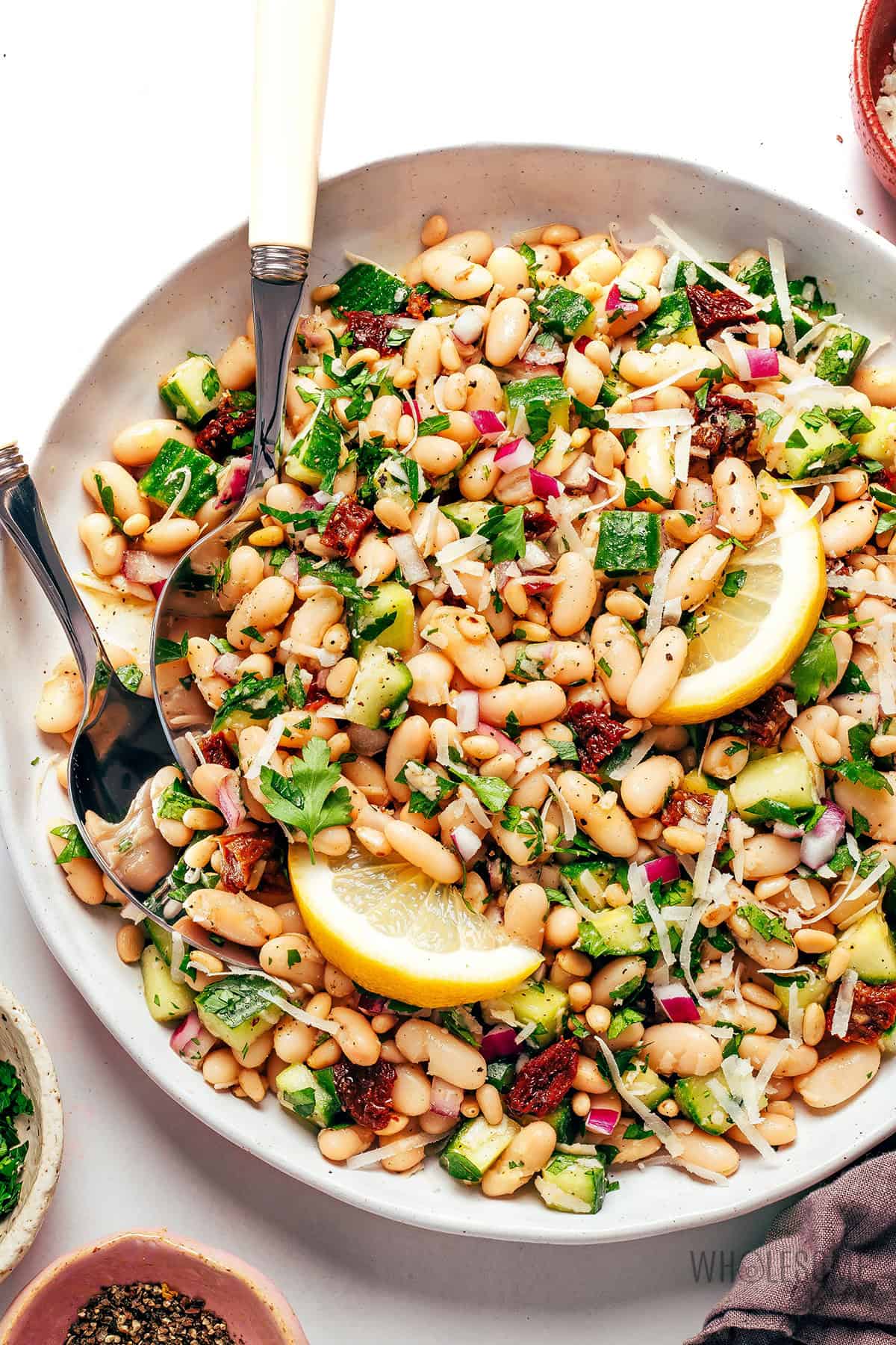 Light and bright white bean salad in a serving bowl with lemons and serving utensils.