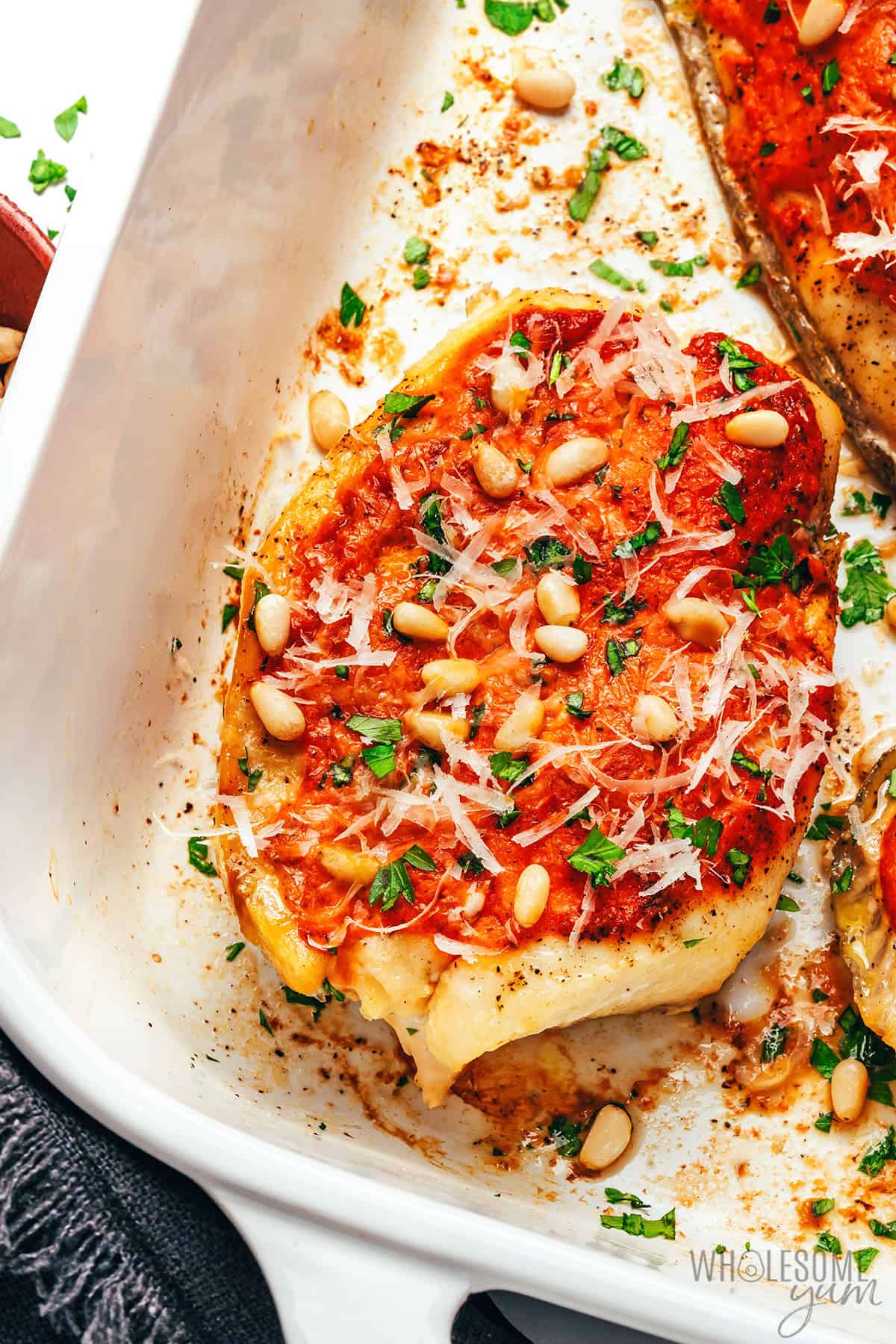 Flavorful baked grouper in a baking dish and garnished with pine nuts, Parmesan cheese, and parsley.