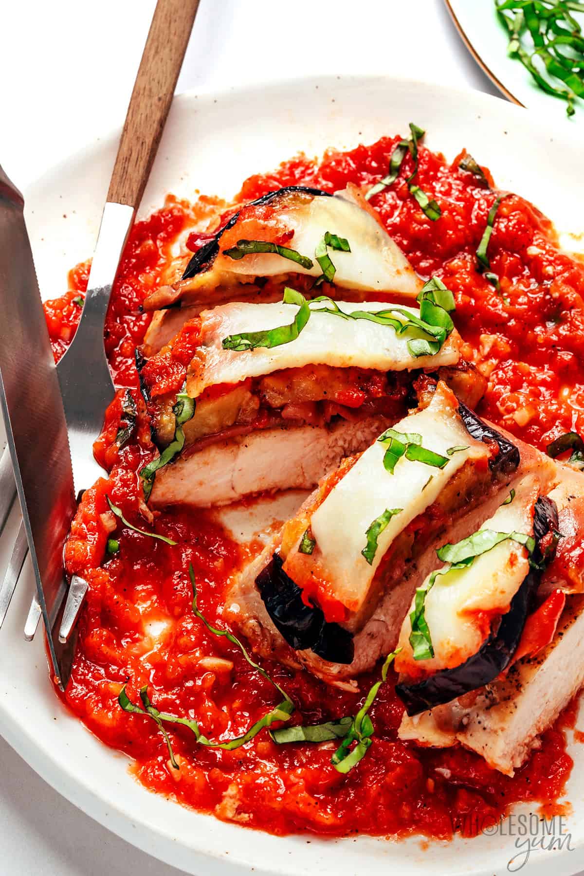 Chicken Sorrentino sliced on a plate with a fork and knife.