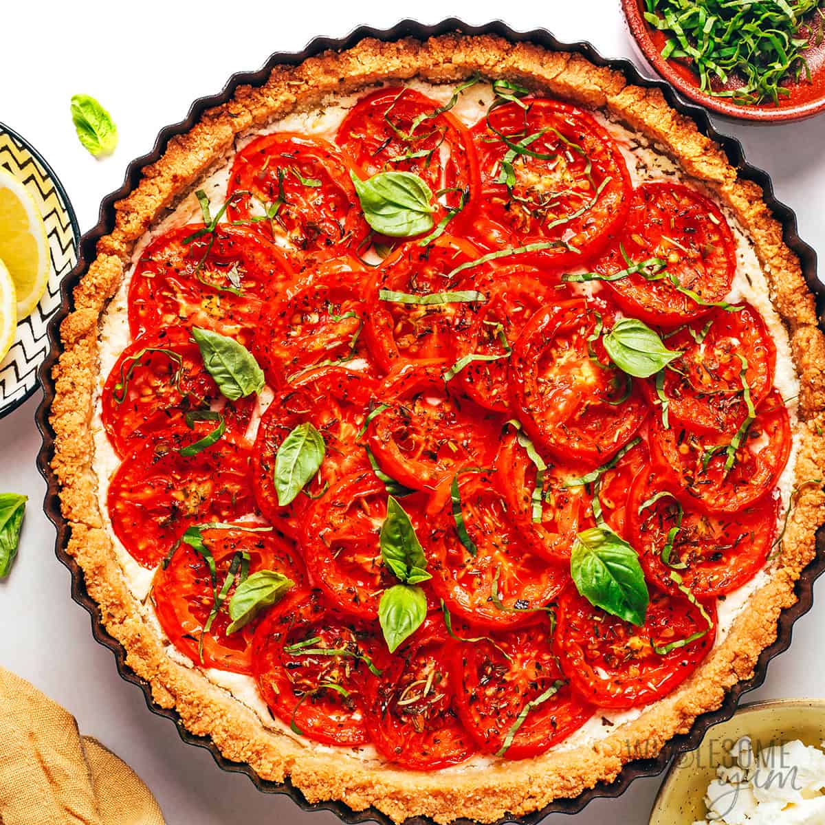 Baked tomato tart recipe topped with fresh basil ribbons and leaves.