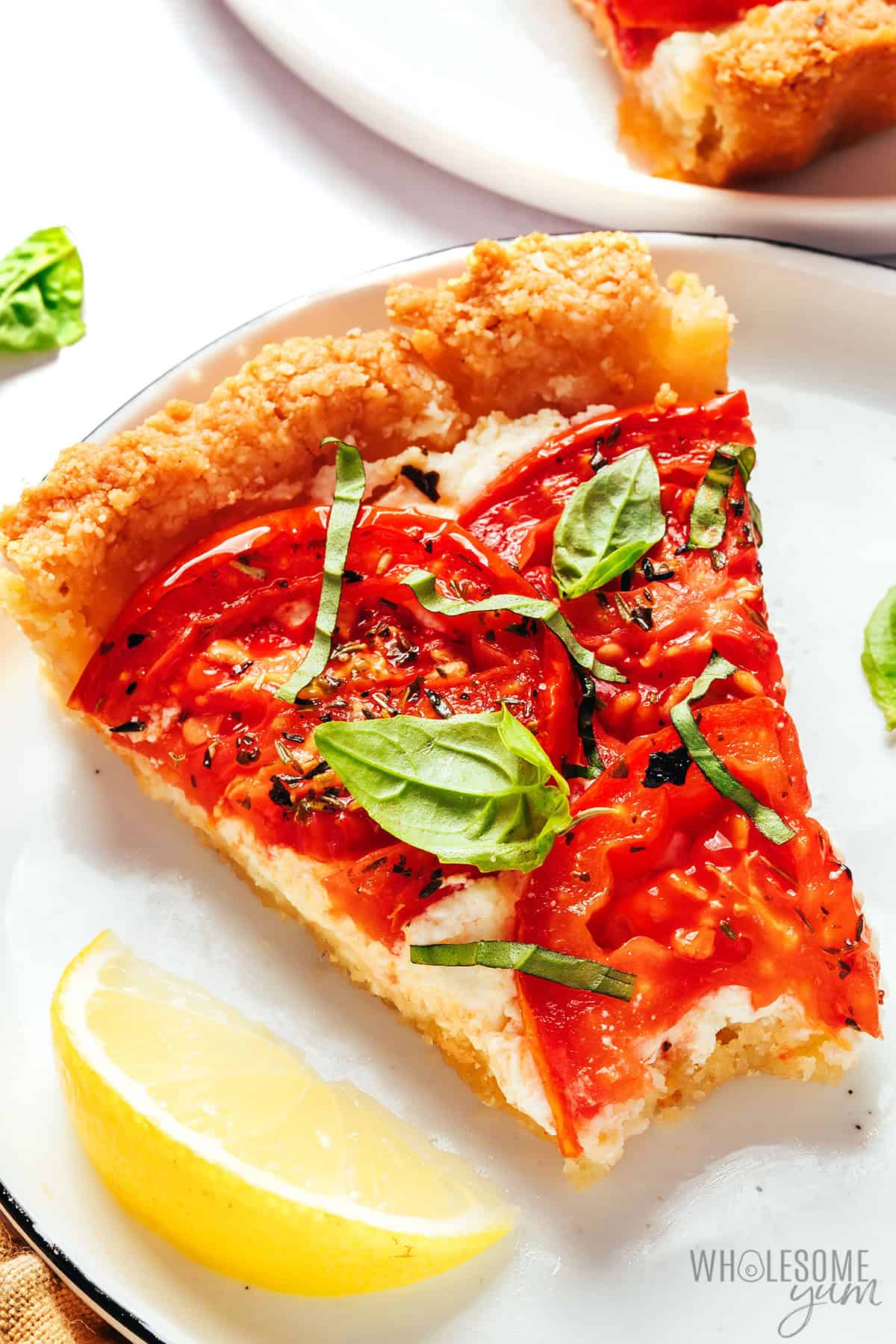 Slice of tomato tart on a plate with a bite removed.