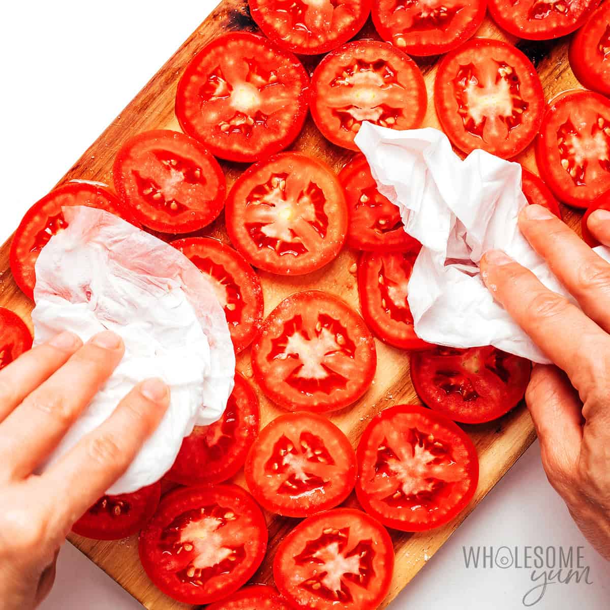 Patting the salted tomato slices dry with paper towels.