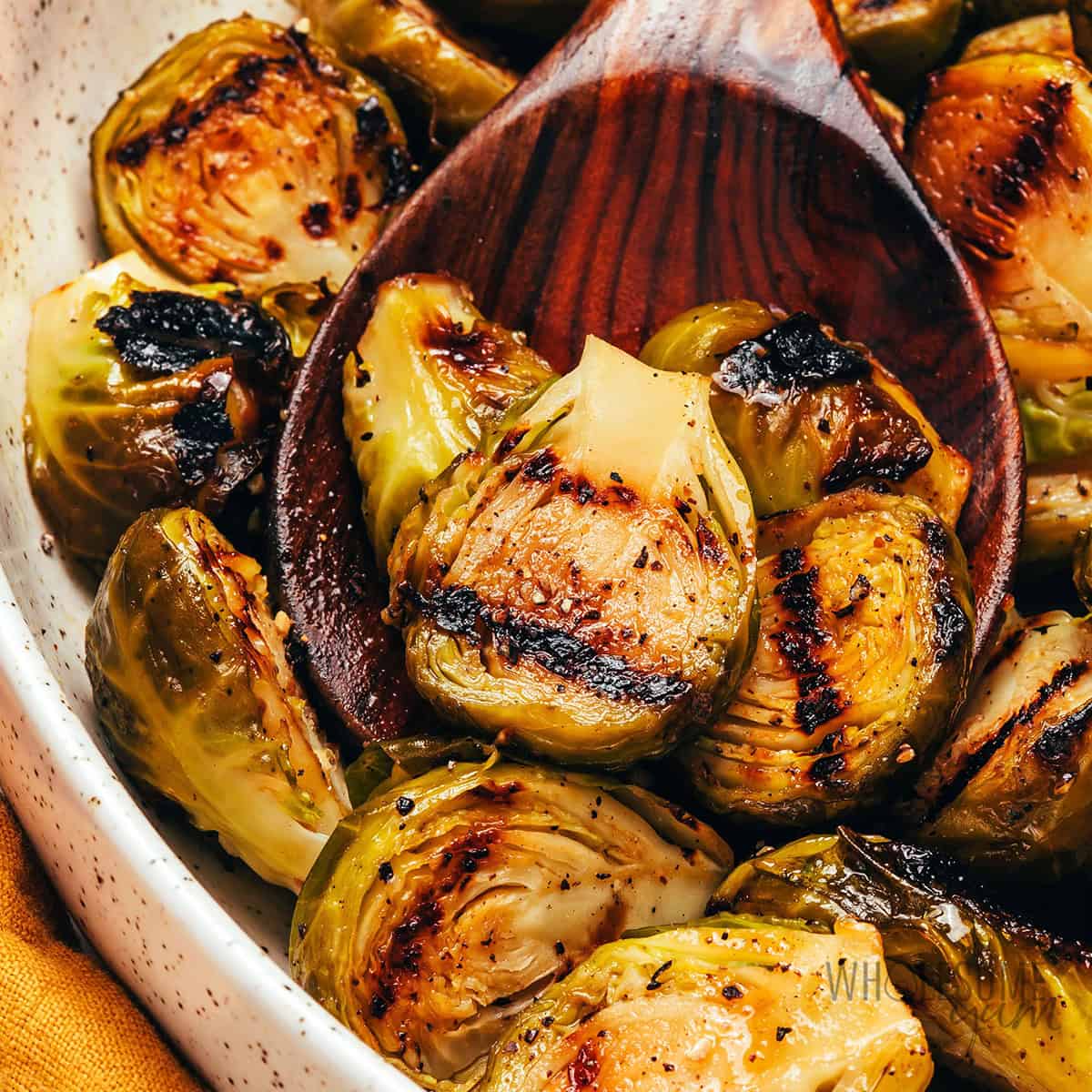 Tender, charred grilled Brussels sprouts in a bowl with a serving spoon.