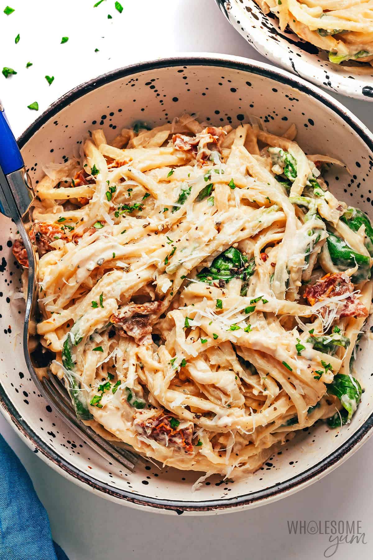 Creamy hearts of palm pasta in a bowl and topped with parmesan cheese.