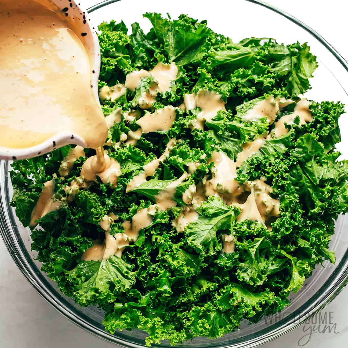 Pouring dressing over kale leaves.